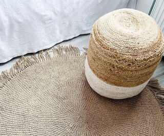Round handwoven two-tone jute pouf styled in a minimalist bedroom.