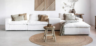 Minimalist scandi interior featuring white sofa, round jute rug, rustic wooden stool and boho cushions.