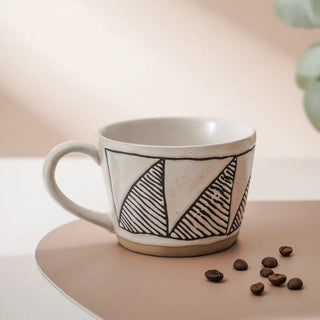 Hand-painted stoneware coffee cup with satin-speckled glaze and graphic motif, styled on a neutral background.