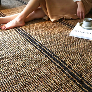 Hand-braided jute and cotton rug with a textured, two-tone weave in soft, neutral beige and black, styled in a modern minimalist interior.