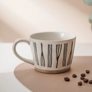 Hand-painted stoneware coffee cup with satin-speckled glaze and graphic motif, styled on a neutral background.