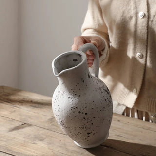 Handmade distressed white ceramic flower vase. The vase features a classic jug shape with a handle and a distressed finish which exudes rustic charm. It complements contemporary, scandi, rustic or boho home décor. A lovely decorative accessory inspired by nature.