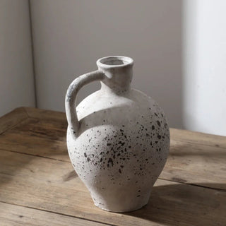 Handmade distressed white ceramic vase. The vase features a classic jug shape with a handle and a distressed finish which exudes rustic charm. It complements contemporary, scandi, rustic or boho home décor. A lovely decorative accessory inspired by nature.