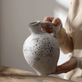 Handmade distressed white ceramic vase. The vase features a classic jug shape with a handle and a distressed finish which exudes rustic charm. It complements contemporary, scandi, rustic or boho home décor. A lovely decorative accessory inspired by nature.