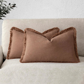 Earthy terracotta cushion cover with fringe trim layered on a modern beige sofa.
