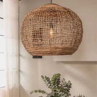 Handwoven abaca pendant light with rounded shape and reclaimed teak top—hanging above a wooden dining table in contemporary interior.