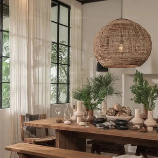 Handwoven abaca pendant light with rounded shape and reclaimed teak top—hanging above a wooden dining table in contemporary interior.