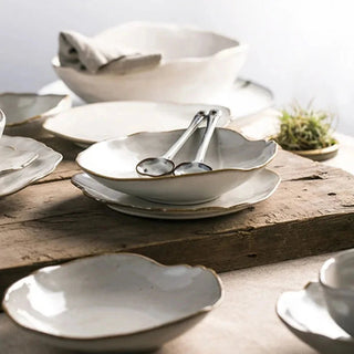 Hand-glazed ceramic plates and bowls with a soft organic shape and hand-painted rim, ideal for serving meals in an elegant, modern table setting.