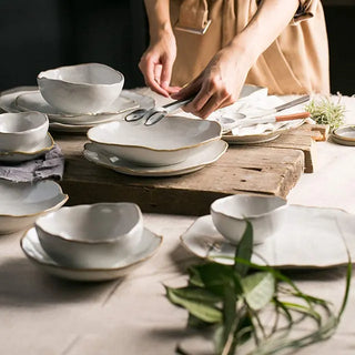 Hand-glazed ceramic plates and bowls with a soft organic shape and hand-painted rim, ideal for serving meals in an elegant, modern table setting.