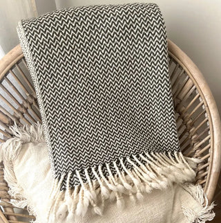 Folded green and white merino wool blanket on rattan chair, breathable natural wool textile.