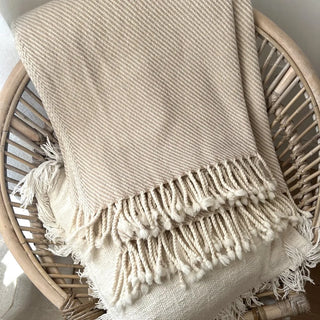Folded beige merino wool blanket on rattan chair, breathable natural wool textile.