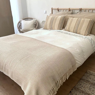 Beige merino wool blanket draped across a bed, natural soft throw for modern interiors.