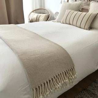 Beige merino wool blanket draped across a bed, natural soft throw for modern interiors.