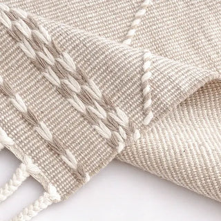 Handwoven beige and white wool rug with geometric kilim pattern and braided fringe for modern, boho and nordic interiors.