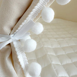 Close-up of a decorative white pom-pom trim on a textured fabric surface.