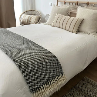 Black and white merino wool blanket draped across a bed, natural soft throw for modern interiors.