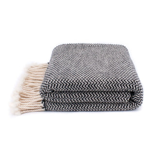 A folded woven blanket with a black and white herringbone pattern and cream-colored fringe tassels.