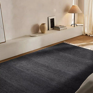 Rectangular black jute rug with fringe detail on light wooden floor