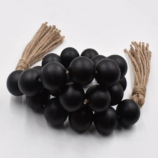 A nature-inspired oversized Wooden Bead Garland, handcrafted from natural wood with a black coating and bold hemp tassels. This rustic, boho décor piece adds relaxed charm to any interior, perfect for styling on trays, plant pots, candle holders, or hanging on walls and doors for a chic, earthy touch.