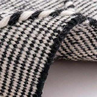 Handwoven black and white wool rug with geometric kilim pattern and braided fringe for modern, boho and nordic interiors.