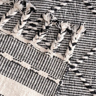 Handwoven black and white wool rug with geometric kilim pattern and braided fringe for modern, boho and nordic interiors.
