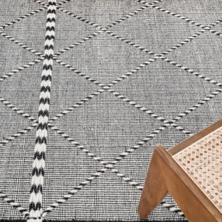 Handwoven black and white wool rug with geometric kilim pattern and braided fringe for modern, boho and nordic interiors.