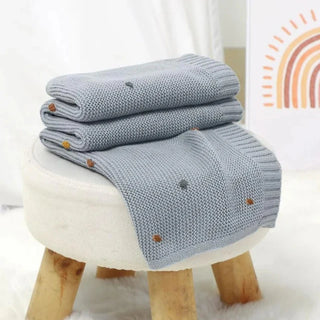 Bibi Cotton Knit Baby Blanket in soft pastel blue, folded neatly on rustic stool.