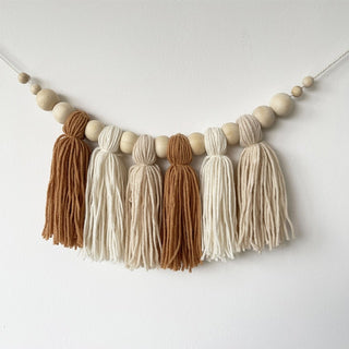Macrame tassel and wooden bead garland in earthy brown, beige, and cream tones for nursery or boho home decor.