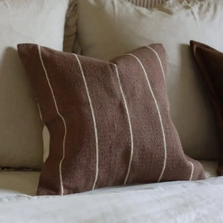 Textured brown accent cushion styled on a bed with neutral bedding and layered cushions.