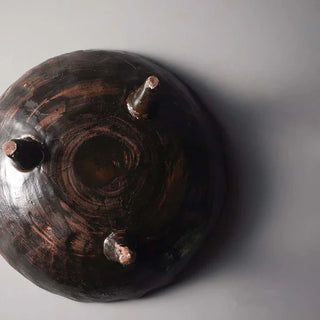 Dark brown handmade ceramic raised dish with a rustic tripod base and textured glaze, ideal for display or styling.