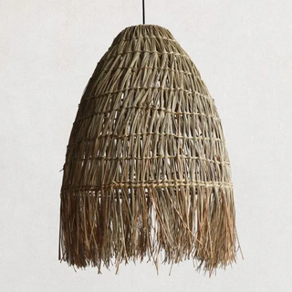 A handwoven rattan and raffia straw pendant light. This natural Cahya pendant lampshade offers a stylish ceiling light, perfect for boho, Scandi, and wabi-sabi home decor. The earthy design enhances any space with its organic charm, making it an ideal choice for natural home decoration and creating a warm, rustic atmosphere. Perfect for adding a unique, sustainable touch to your living room, dining room, or bedroom lighting.