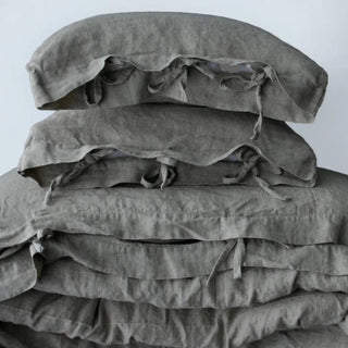 Light grey linen bedding set with tie closures, styled on a bed with two pillows and a cozy duvet, creating a calm, minimalist bedroom look.