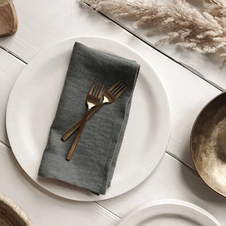 Charcoal linen table napkins set on wooden dining table with minimalist tableware.