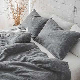 Pure linen pillowcase set in dark grey, styled with matching duvet and sheets in a minimalist bedroom.