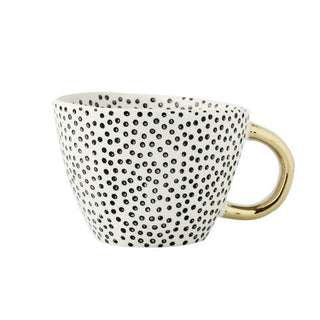 Handmade white ceramic cup with black dots and a gold handle, minimalist and artistic in style.
