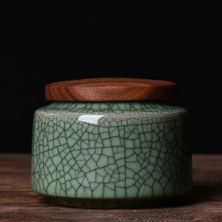 Elegant crackled glaze ceramic storage canister with a dark walnut lid, perfect for kitchen or home organization. Featuring a textured, artisanal design in a soft green hue, this airtight container is ideal for storing tea, coffee, spices, or small household items. A stylish and functional addition to natural homeware collections.