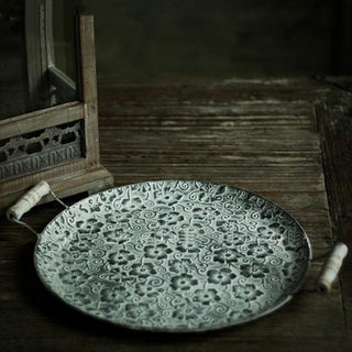 Round floral embossed galvanized iron tray, a stylish metal serving plate with handles perfect for kitchen tableware. This durable serving plate features intricate embossing, adding a touch of elegance to your dining experience. Ideal for both practical use and natural home decor, it enhances your table setting with rustic charm and versatility.