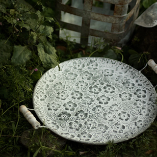 Round floral embossed galvanized iron tray, a stylish metal serving plate with handles perfect for kitchen tableware. This durable serving plate features intricate embossing, adding a touch of elegance to your dining experience. Ideal for both practical use and natural home decor, it enhances your table setting with rustic charm and versatility.