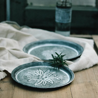 Round embossed galvanized iron tray, a stylish metal serving plate perfect for kitchen tableware. This durable serving plate features intricate embossing, adding a touch of elegance to your dining experience. Ideal for both practical use and natural home décor, it enhances your table setting with rustic charm and versatility.
