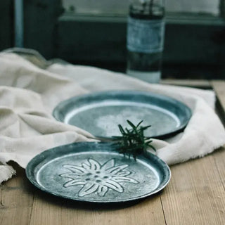 Rustic round galvanised iron serving tray with floral embossing, ideal for bread, cheese, or decorative tabletop styling.