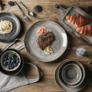 Black and grey porcelain bowls and plates with a stoneware-style matte texture, minimal design, and artisanal finish, ideal for serving soup, salad and mains.