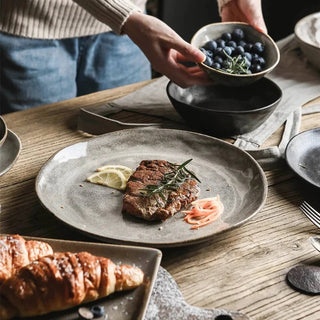 Black and grey porcelain bowls and plates with a stoneware-style matte texture, minimal design, and artisanal finish, ideal for serving soup, salad and mains.