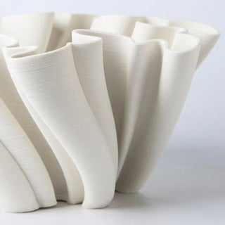 A sculptural, white decorative centerpiece bowl with an intricate, undulating design. The bowl's structure features twisted, fluted elements that create a dynamic, flowing appearance. The design is modern and minimalist, adding an artistic touch to home décor.