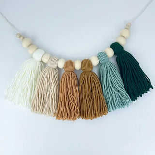 Macrame tassel and wooden bead garland in earthy green, clay, and cream tones for nursery or boho home decor