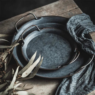 Round galvanized iron tray, a stylish metal serving plate with handles perfect for kitchen tableware. This durable serving is durable and ideal for both practical use and natural home decor, it enhances your table setting with rustic charm and versatility.