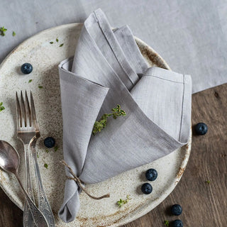 Soft grey linen napkins styled with a rustic ceramic plate on a wooden dining table.