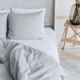 Close up of a light grey linen bedding set styled on a bed with two pillows and a cozy duvet, creating a calm, minimalist bedroom look.