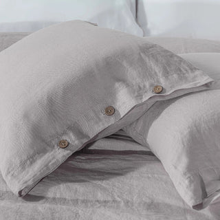 Grey linen pillowcases with coconut button closures on a bed.