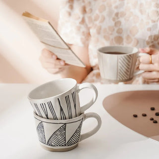 Hand-painted stoneware coffee cup with satin-speckled glaze and graphic motif, styled on a neutral background.