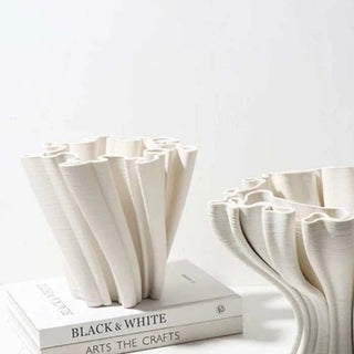 A sculptural, white decorative centerpiece bowl with an intricate, undulating design. The bowl's structure features twisted, fluted elements that create a dynamic, flowing appearance. The design is modern and minimalist, adding an artistic touch to home decor.